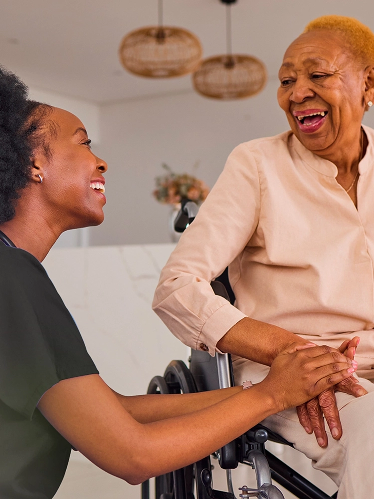 Home healthcare nurse holding hands with senior woman in wheelchair during in-home care visit