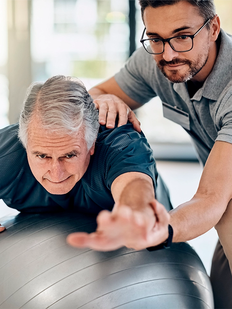 Physiotherapist assisting senior man with balance exercise on stability ball during in-home rehabilitation