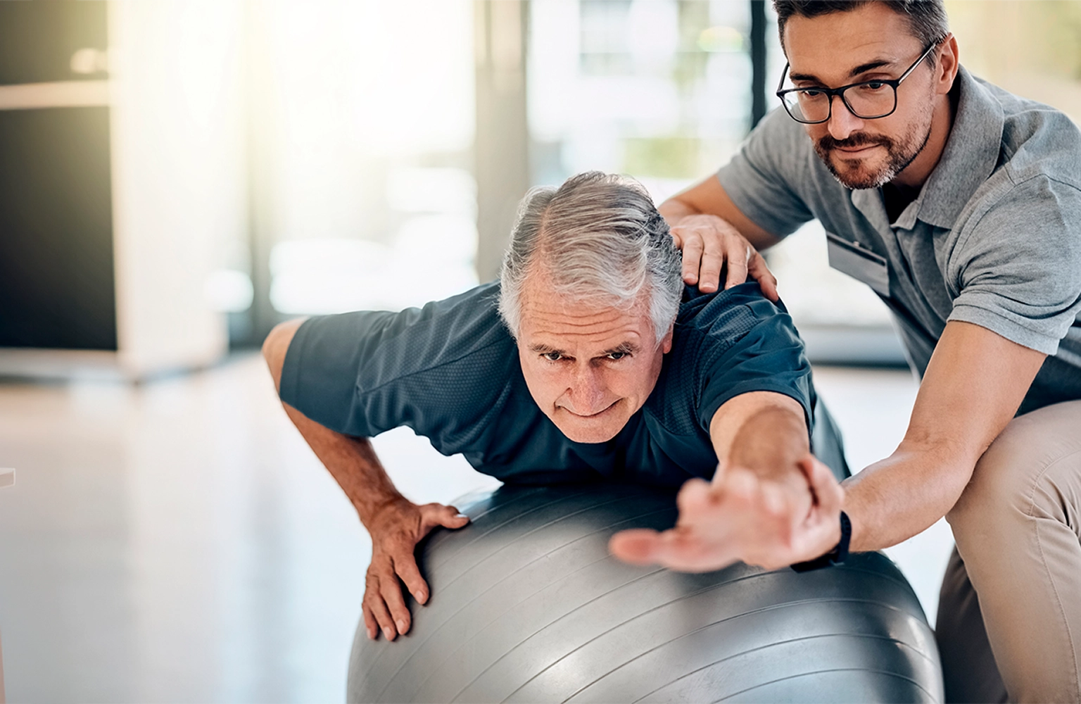 Physiotherapist assisting senior man with balance exercise on stability ball during in-home rehabilitation
