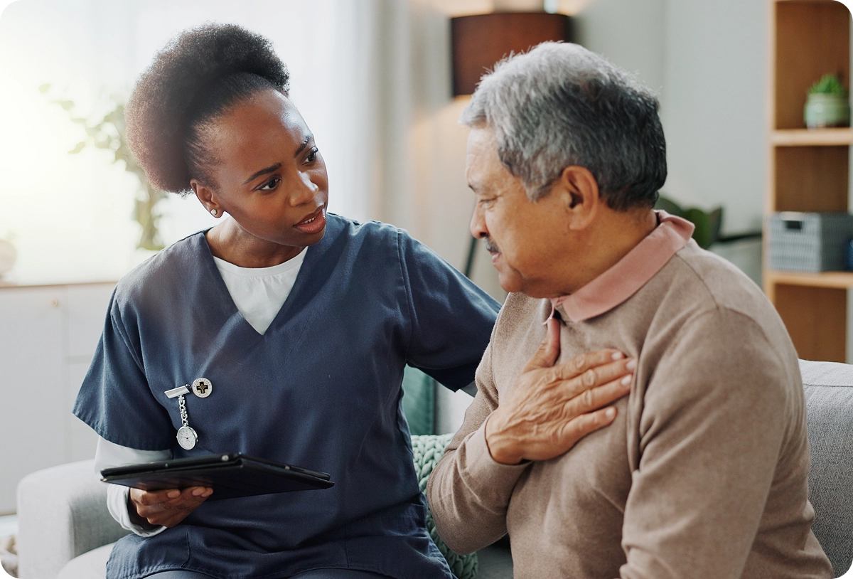 A nurse in dark blue scrubs sitting with a senior resident, discussing medical care options and providing support.